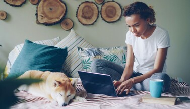 Frau mit Laptop und Hund zuhause.