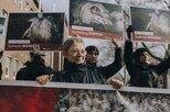 Frau hinter einem Banner, auf dem zahllose Mastputen zu sehen sind. Hinter ihr Menschen mit Schildern, auf denen leidende Mastputen und die Claims 