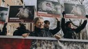 Frau hinter einem Banner, auf dem zahllose Mastputen zu sehen sind. Hinter ihr Menschen mit Schildern, auf denen leidende Mastputen und die Claims 