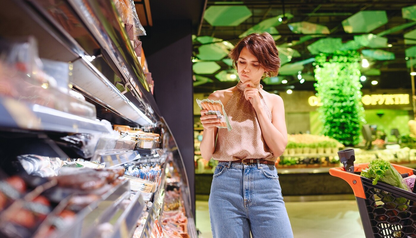 Junge Frau im Supermarkt studiert die Verpackung von Würstchen.