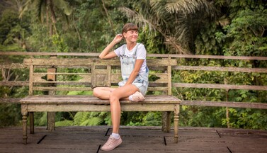 Frau auf einer Bank vor tropischen Pflanzen.